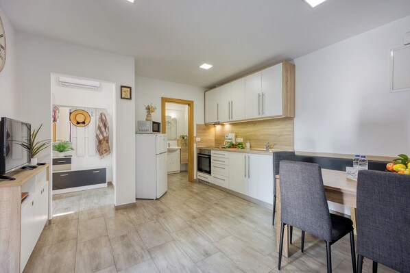 A modern kitchen with white cabinets, a wooden countertop, and a dining area with grey chairs.