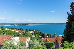 A coastal town with terracotta-roofed houses, a clear blue sea, and a distant shoreline.
