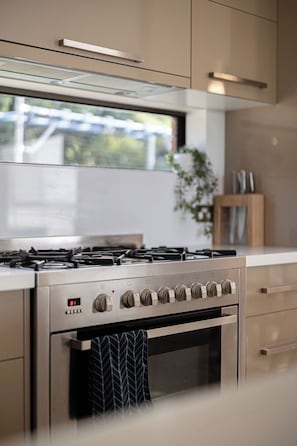 A modern kitchen with a stainless steel stove, a range hood, and a window with a view of greenery outside. - Valley View Home | Sauna, Fire Pit, Pizza Oven (Port Lincoln)