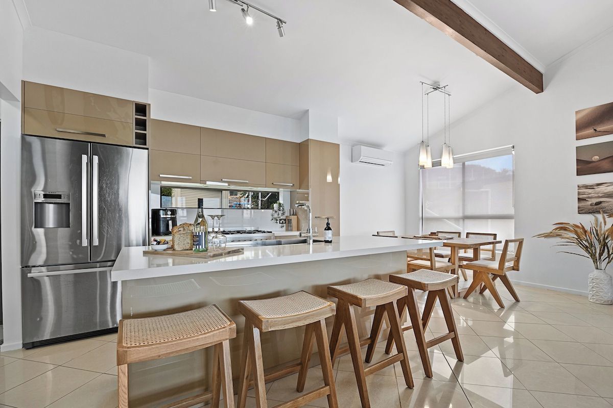 Une cuisine moderne dotée d’un réfrigérateur en acier inoxydable, de tabourets de bar en bois et d’un grand îlot central.