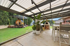 Expansive outdoor entertaining area featuring a wood fired pizza oven, private barrel sauna, open lawn space and covered alfresco dining designed for relaxed coastal living.