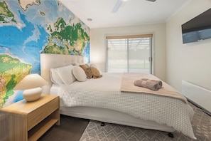 A bedroom with a large world map on the wall, a bed with a white comforter, a wooden nightstand with a lamp, and a TV mounted on the wall. - Valley View Home | Sauna, Fire Pit, Pizza Oven (Port Lincoln)