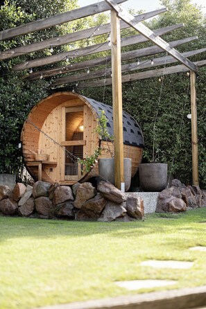 A wooden cabin with a curved roof, a stone wall in front, and a pergola overhead. - Valley View Home | Sauna, Fire Pit, Pizza Oven (Port Lincoln)