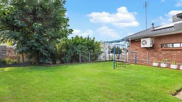 A backyard with a swing set, a brick house, and a large tree.