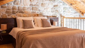 Een slaapkamer met een stenen muur, houten plafond en een bed met veel kussens.