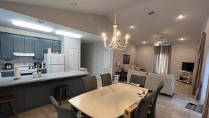 A modern kitchen with a central island, dining area with chairs, and a living space with a sofa and TV. - Point Fourchon Unit D (Golden Meadow)