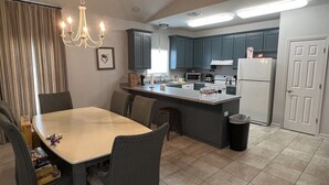 A modern kitchen with dark cabinets, a central island, and a dining area with chairs. - Point Fourchon Unit D (Golden Meadow)