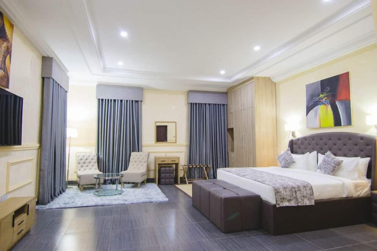 A hotel room with a large bed, a desk, two chairs, a small table, and a TV.