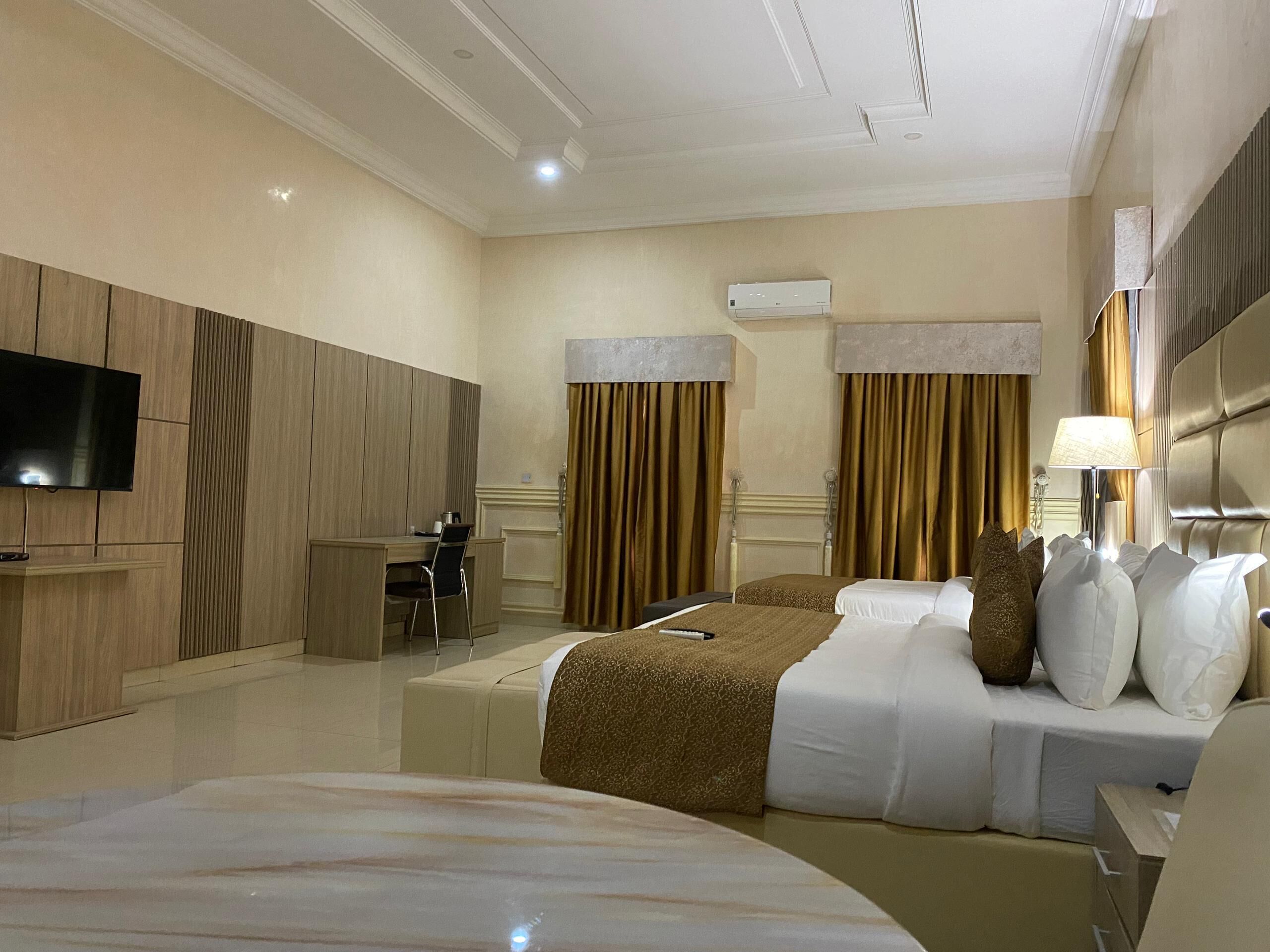 Habitación de hotel con una cama grande, una cama más pequeña, un escritorio, una silla, un televisor y una ventana con cortinas.