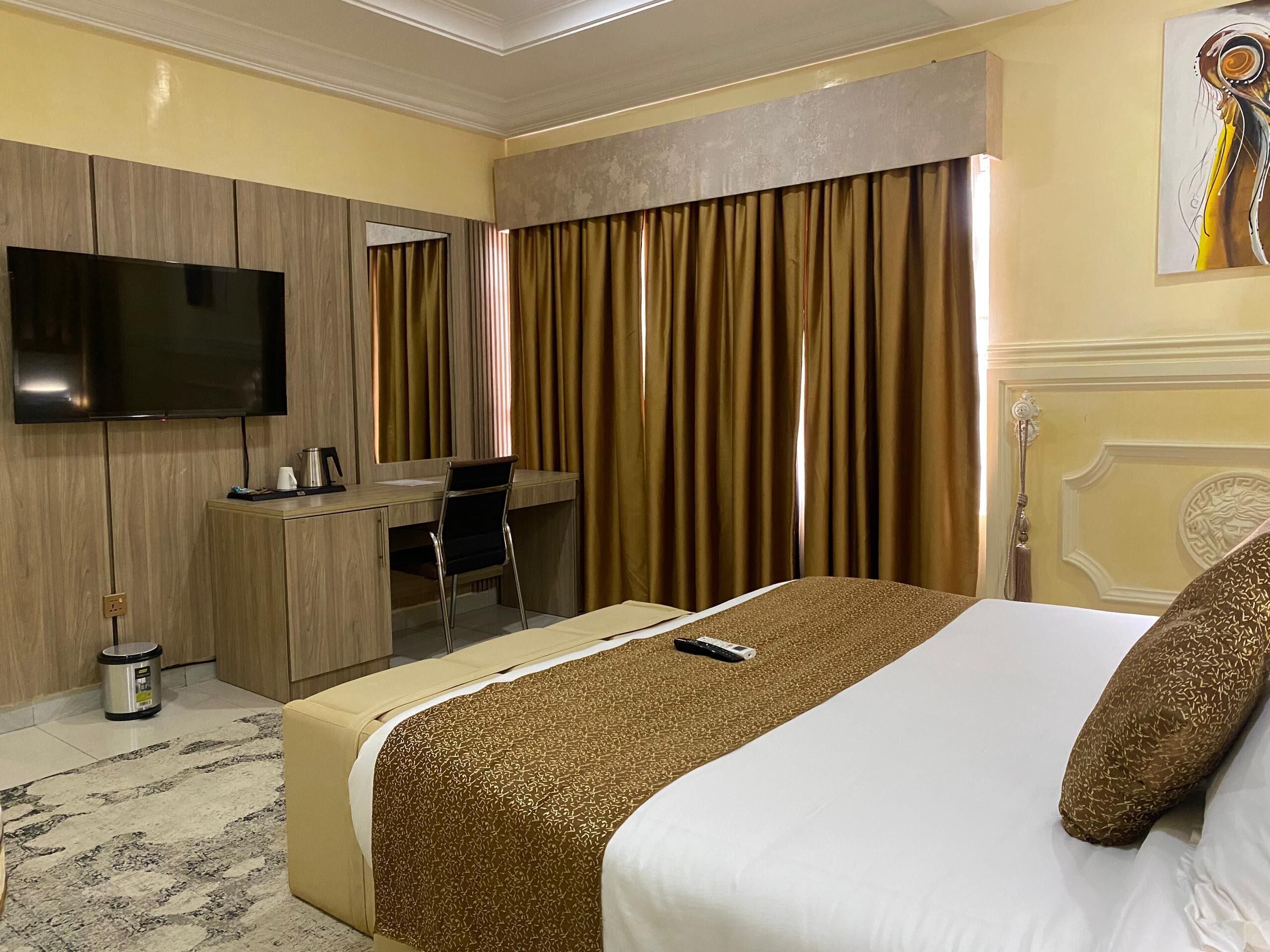 A hotel room with a bed, a desk with a chair, a television, and a painting on the wall.