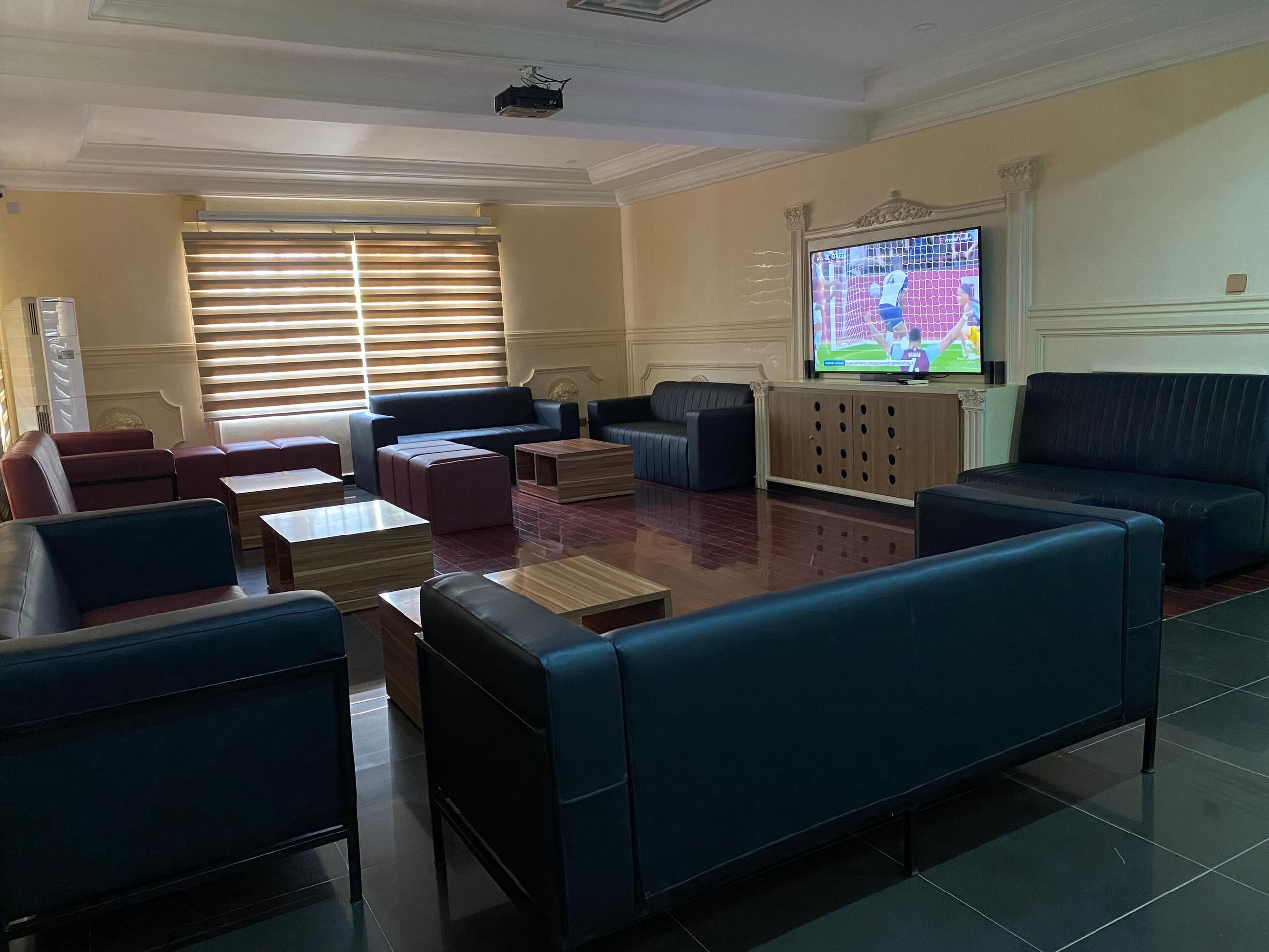 A spacious living room with multiple seating areas, a large flat-screen TV, and a ceiling projector.