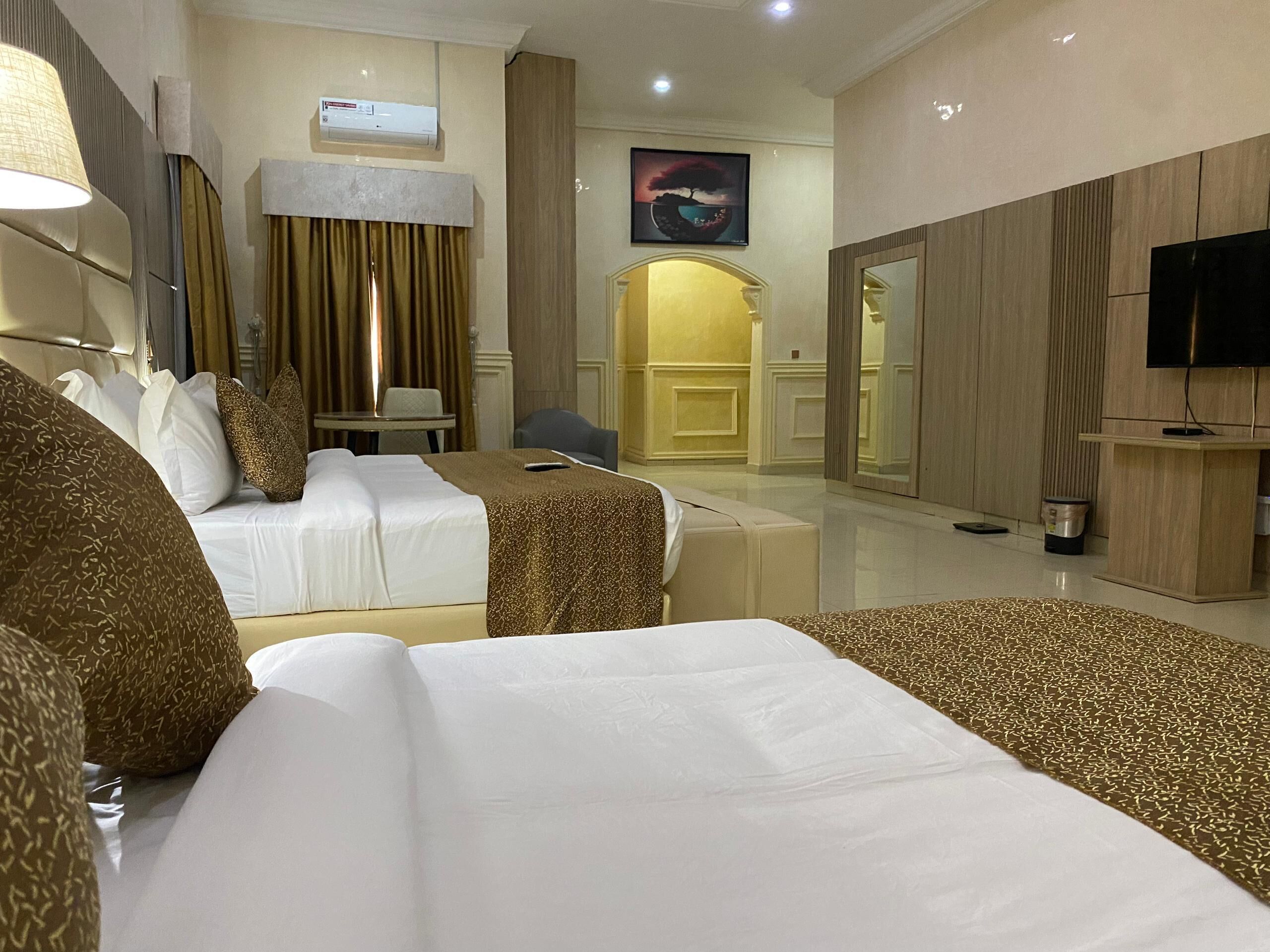 A hotel room with two beds, a desk, a chair, a TV, and a painting on the wall.