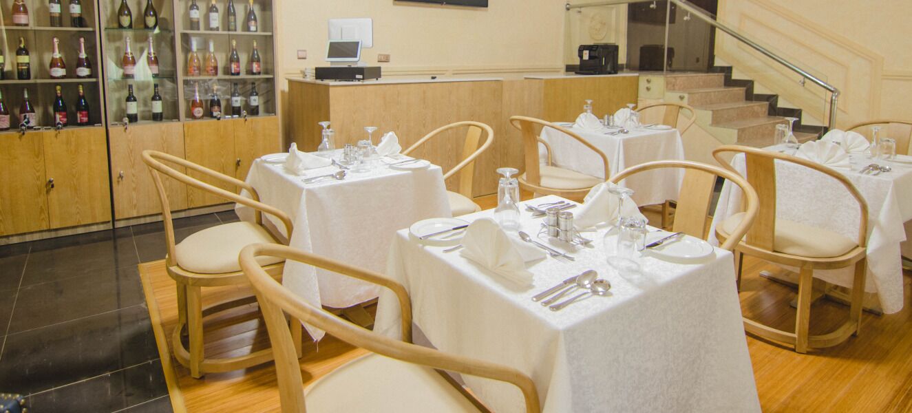 Una sala ristorante con diversi tavoli apparecchiati, ognuno con tovaglioli bianchi e posate disposte con cura.