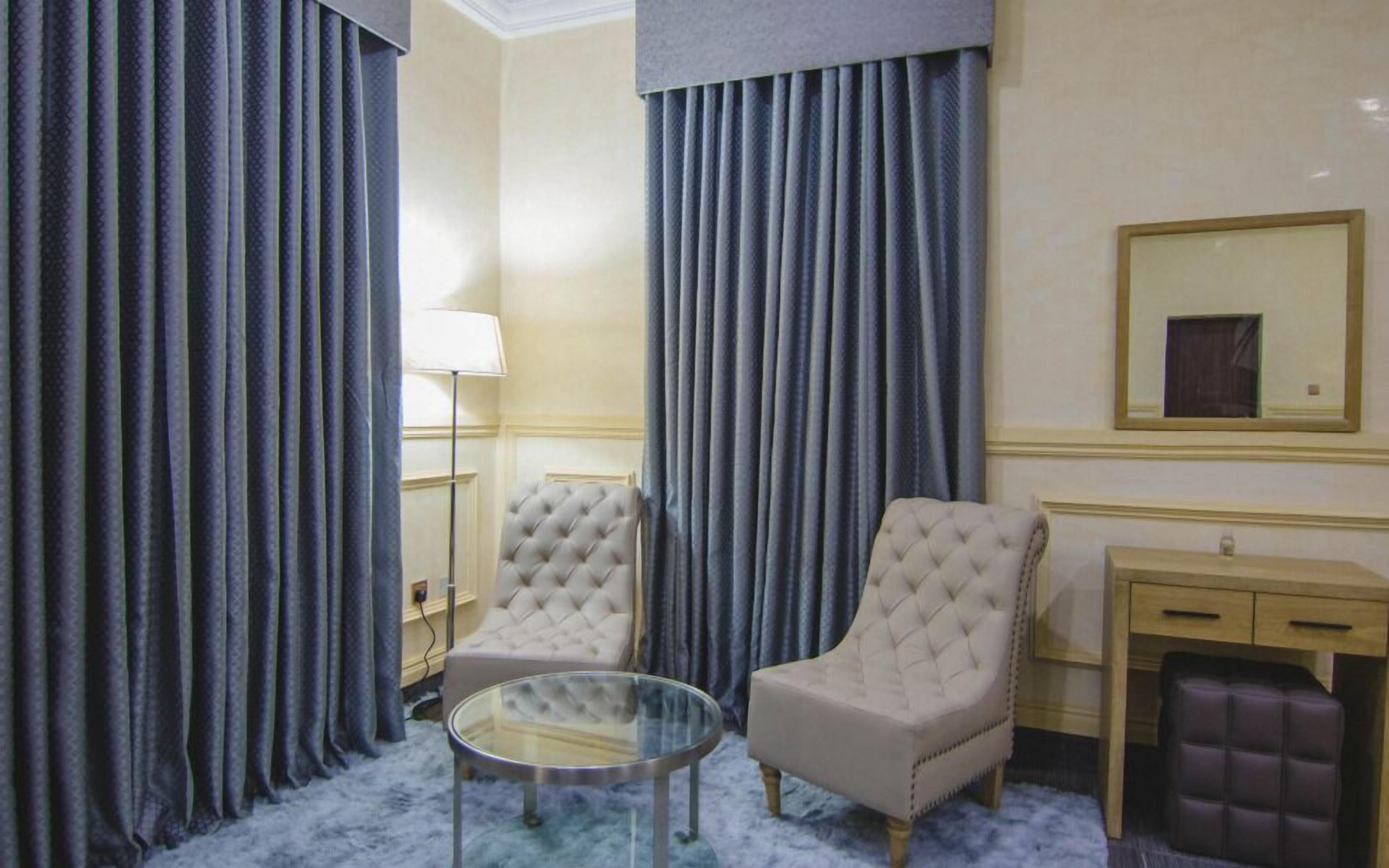 Een kamer met twee fauteuils, een glazen salontafel, een lamp en een spiegel aan de muur.