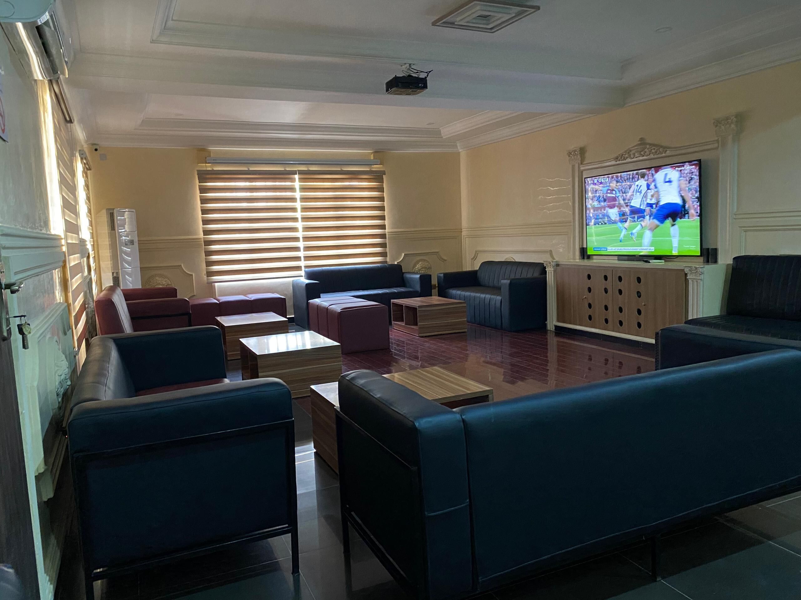 A hotel lobby with seating areas, a television, and a large window with blinds.