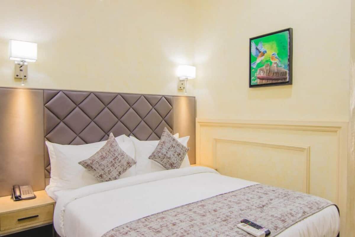 A neatly made bed with a tufted headboard, two bedside lamps, a bedside phone, and a painting on the wall.