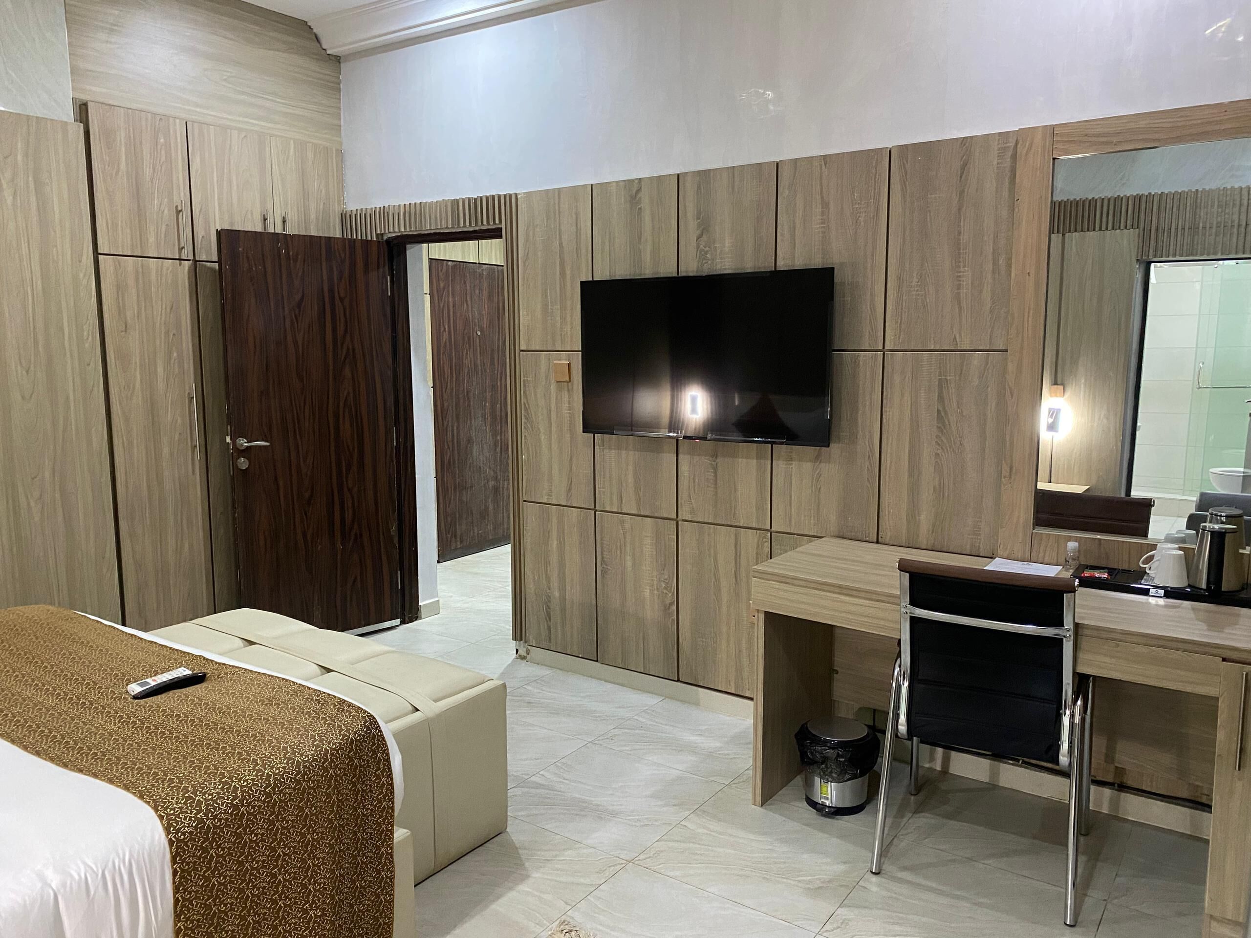 A modern hotel room with a bed, a TV mounted on the wall, a desk with a chair, and a small trash bin.