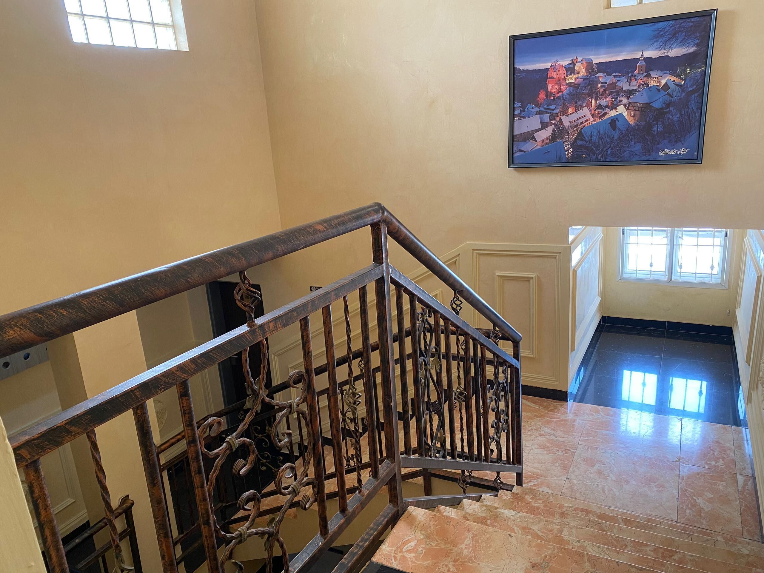 A staircase with ornate metal railings and a cityscape painting on the wall.