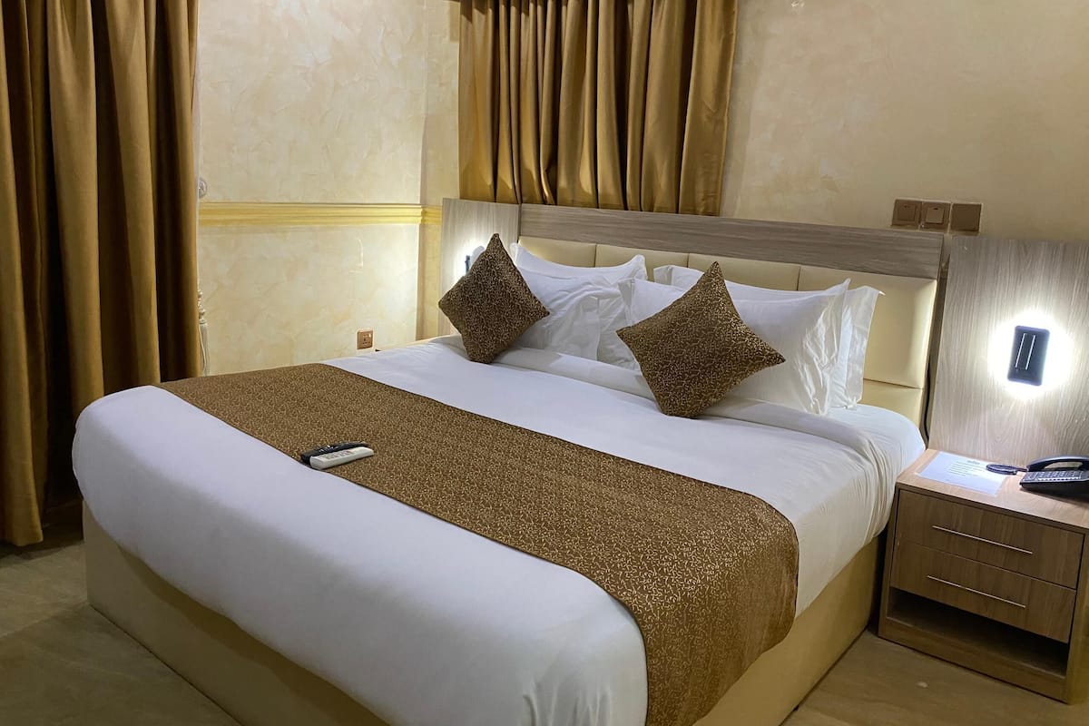 A hotel room with a large bed, two pillows, a bedside table with a phone, and a wall-mounted light.