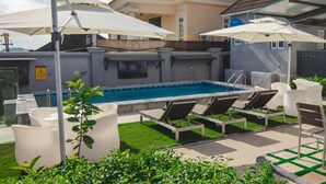 Un espace aménagé au bord de la piscine, avec des chaises longues, des parasols et une piscine.