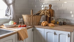 A kitchen with a checkered tablecloth, a basket of fresh produce, jars of spices, and a wooden cutting board. - MAJADA DEL CONDE (La Guardia)