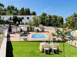 Zona de piscina con mesa lista para comer, rodeada de vegetación y un parque infantil.