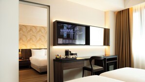 A hotel room with a bed, a desk with a chair, a television mounted on the wall, and a window with curtains.