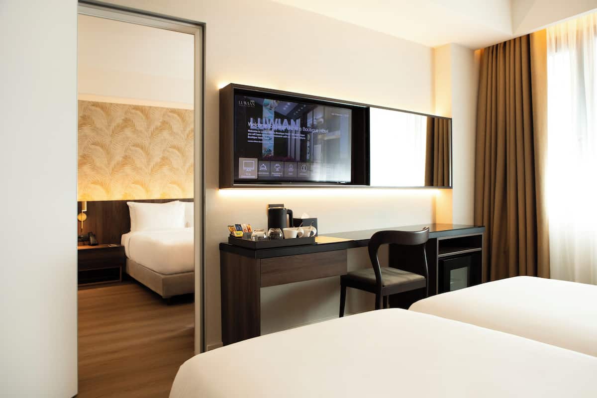 Habitación de hotel con cama, escritorio y silla, televisor montado en la pared y ventana con cortinas.