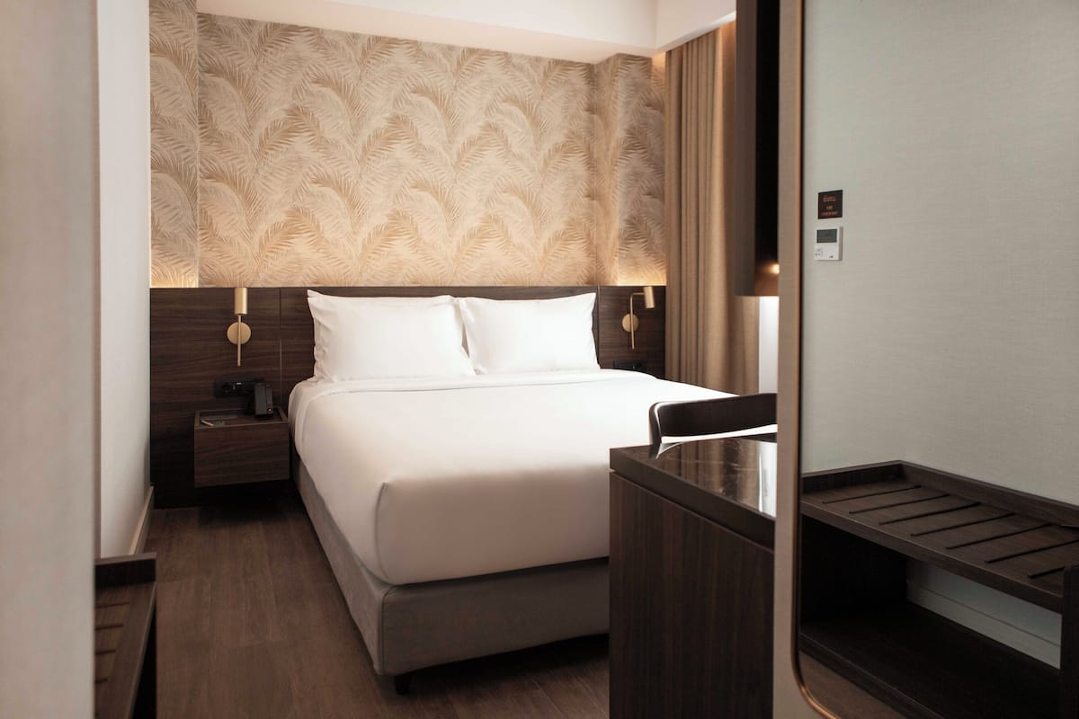 Una habitación de hotel con una cama grande, una mesita de noche, una lámpara de pared y un banco de madera.