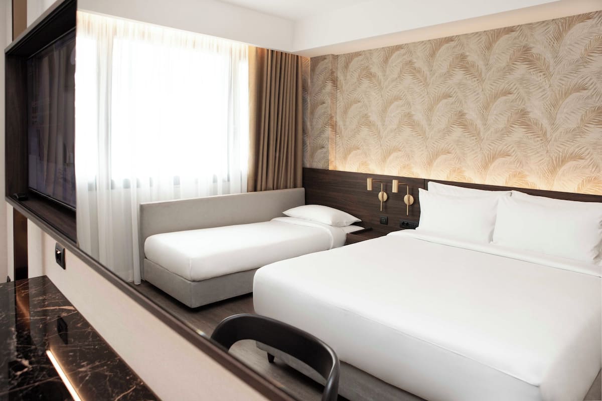 Habitación de hotel con una cama grande, una cama más pequeña, un televisor y un escritorio.