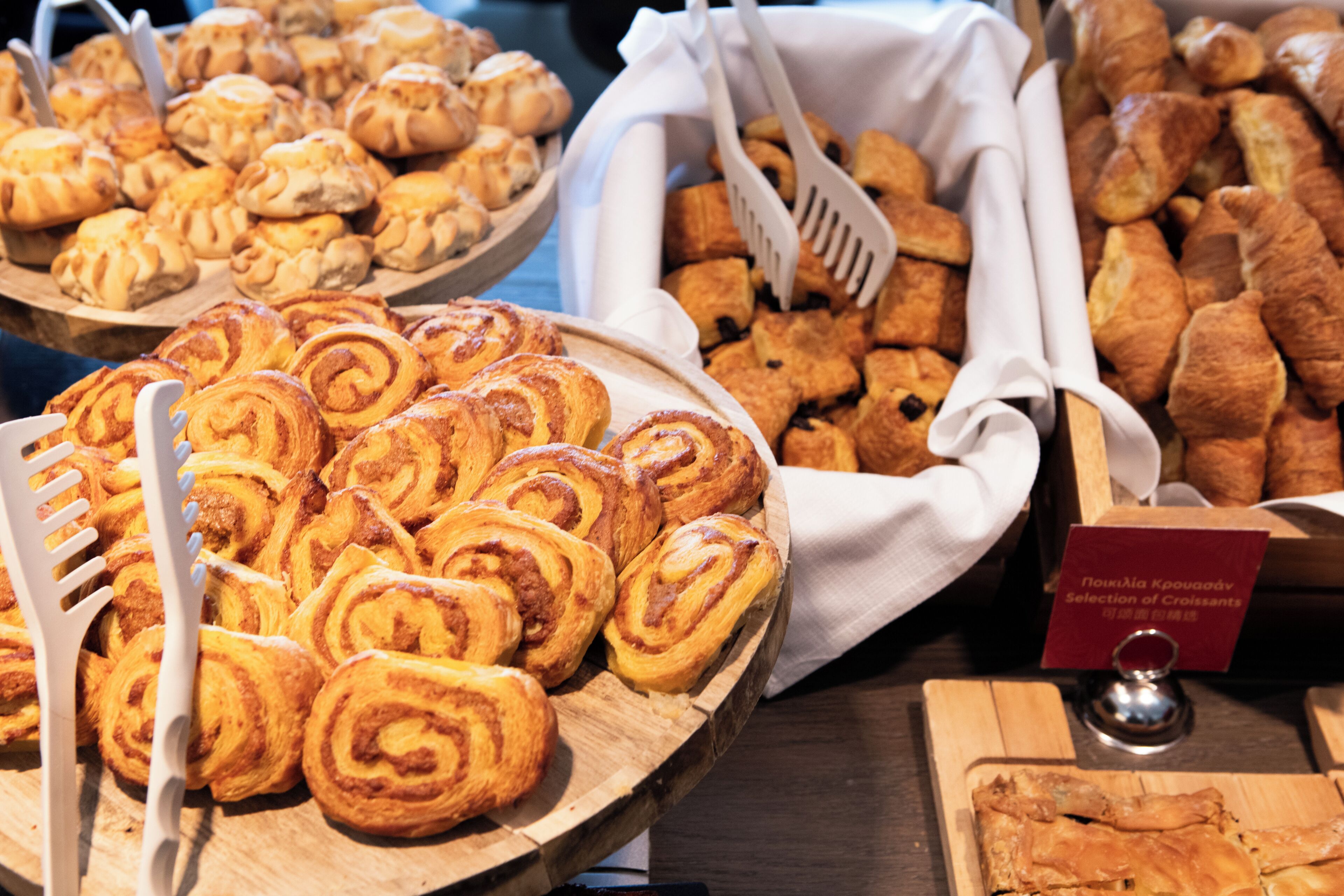 A variety of pastries on wooden trays with serving utensils.