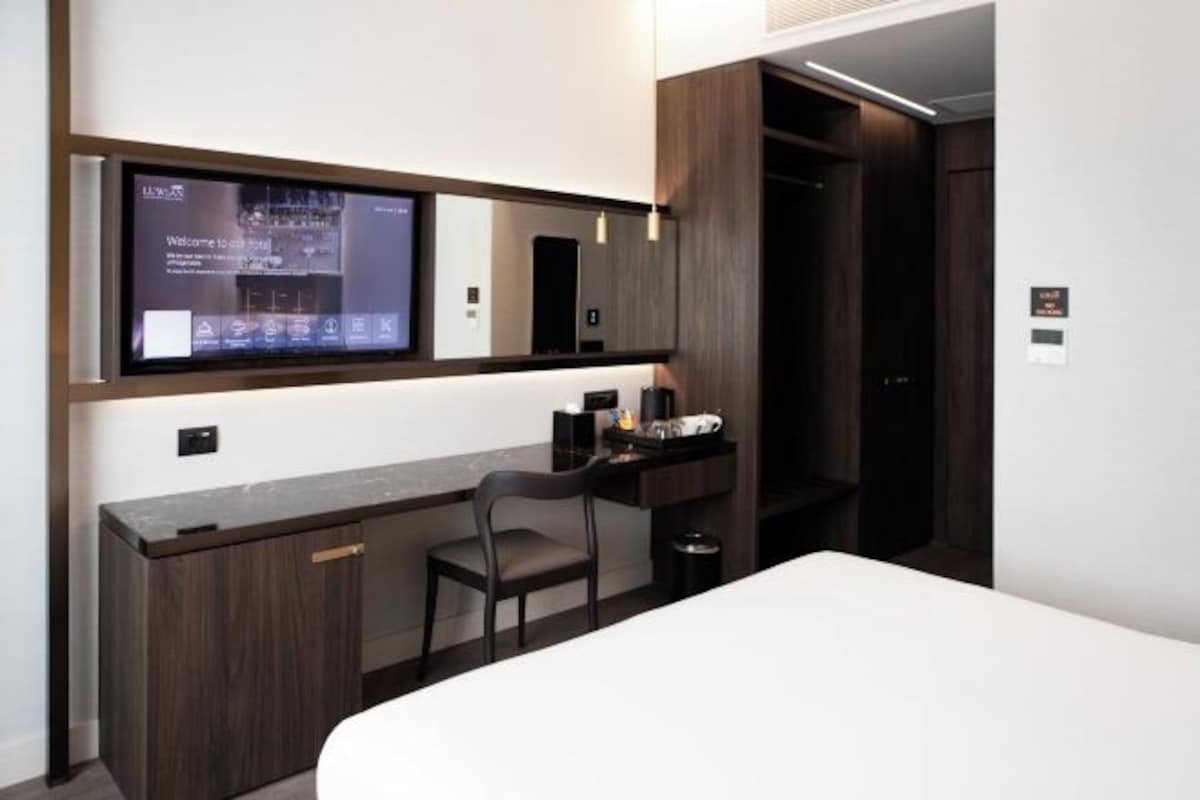 Habitación de hotel con cama, escritorio con silla, televisión en la pared y armario.