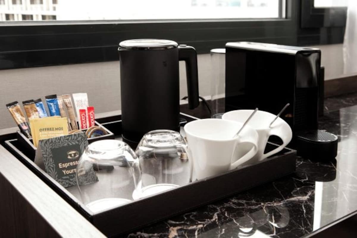 Una estación de café con una bandeja que contiene una cafetera, tazas y sobres de café.