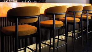 A bar area with multiple bar stools, a counter with a lighted bar, and a patterned wall in the background.