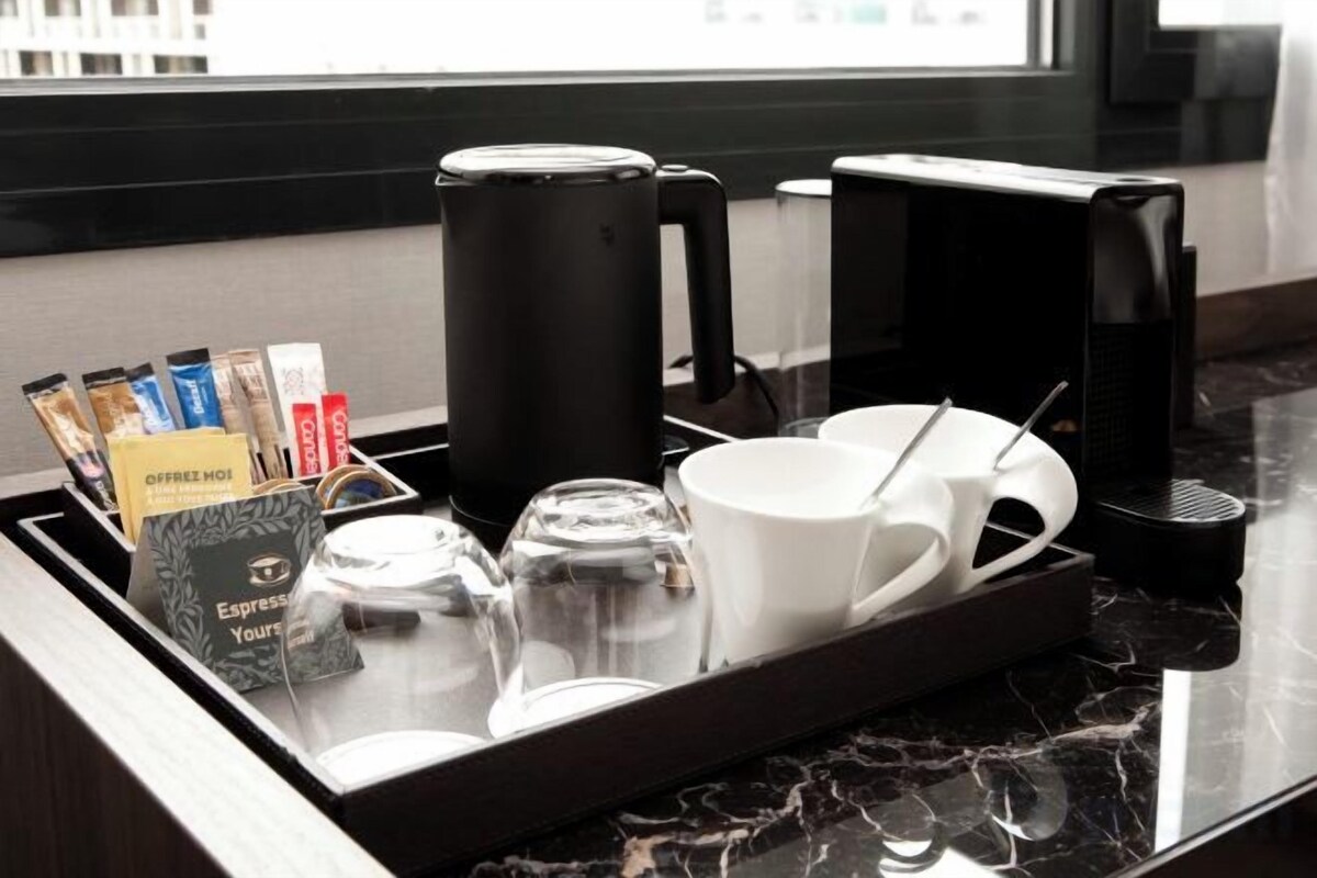 Una estación de café con una bandeja que contiene una cafetera, tazas y sobres de café.
