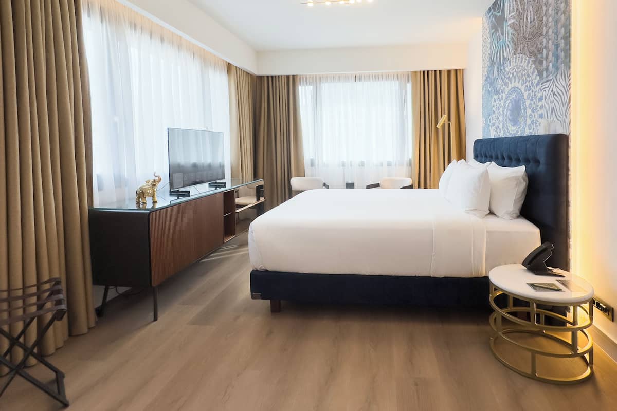 Habitación de hotel con cama, escritorio con televisor, una silla y una mesita.