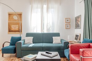 A modern living room with a teal sofa, a red leather chair, and a coffee table with a book and remote control.