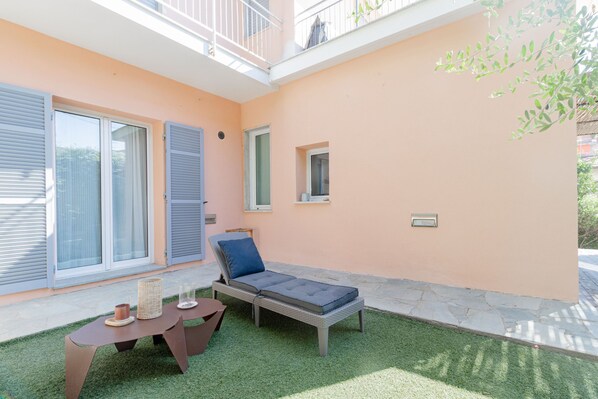 A small outdoor seating area with a table and chairs, a cushioned lounge chair, and a small window.