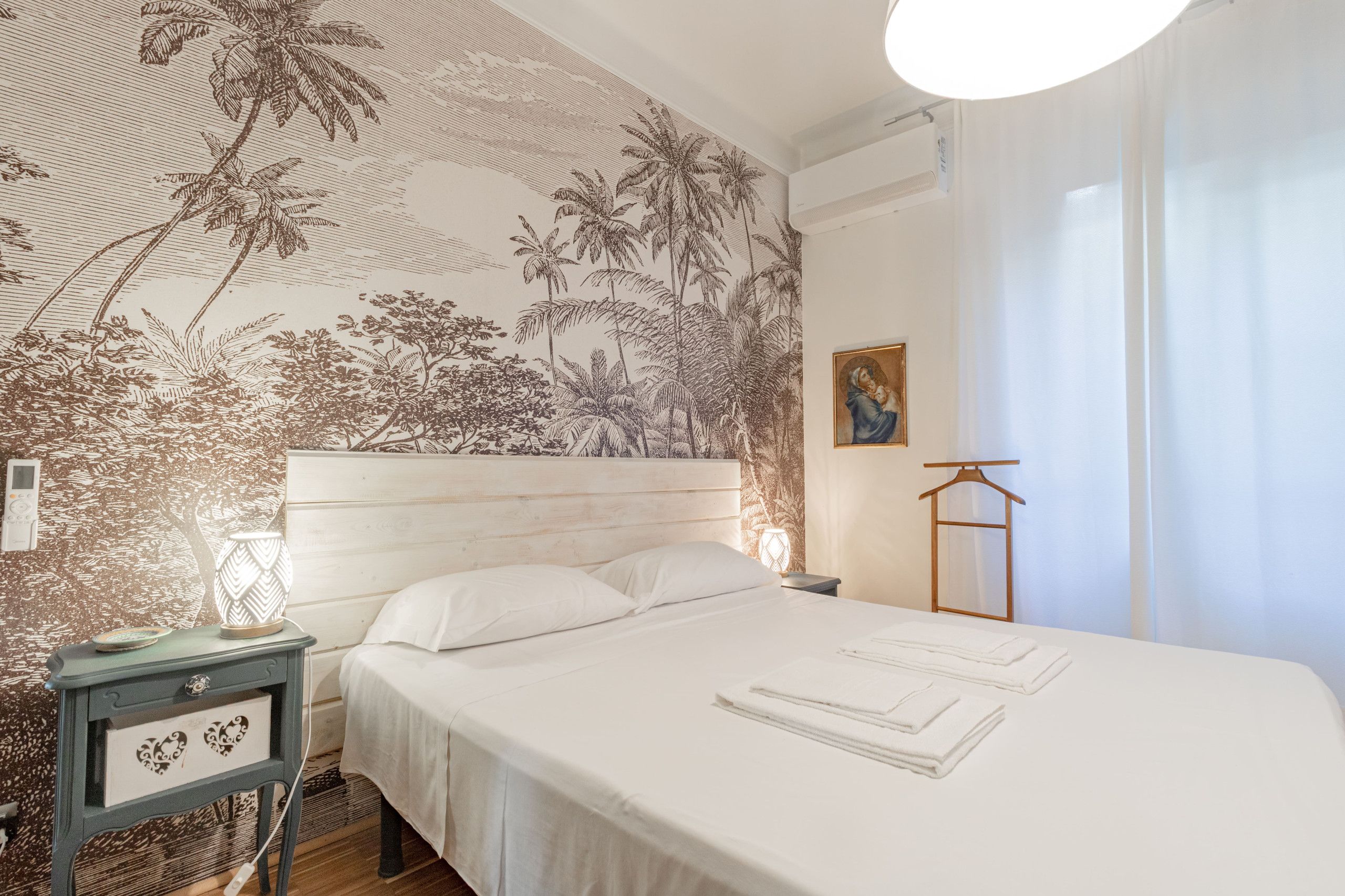 Une chambre à coucher comprenant un lit, une table de chevet, une lampe, un climatiseur fixé au mur et un tableau.