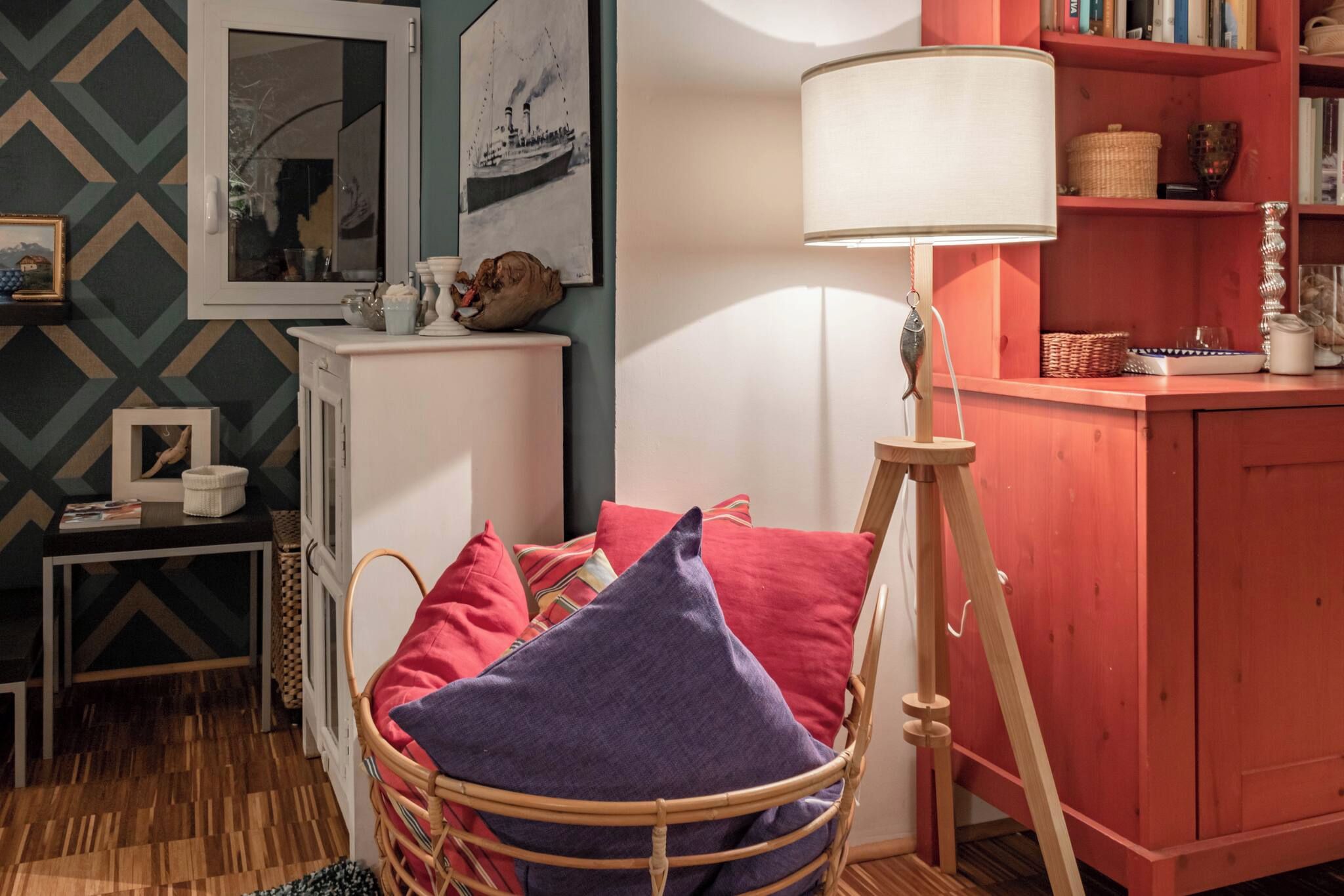 Une pièce chaleureuse avec un fauteuil en osier, une lampe blanche et une bibliothèque.