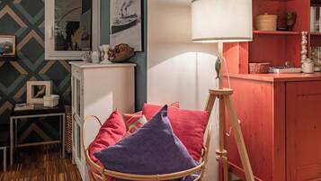 Une pièce chaleureuse avec un fauteuil en osier, une lampe blanche et une bibliothèque.