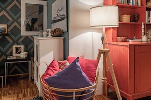 A cozy room with a wicker chair, a white lamp, and a bookshelf.