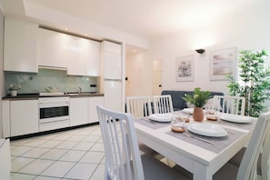 Una cocina moderna con armarios blancos, una mesa de comedor dispuesta para cuatro personas y una planta en maceta sobre la mesa.