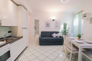 Un espacio habitable compacto con kitchenette, un sofá, una mesa de comedor para dos comensales y una planta en maceta.