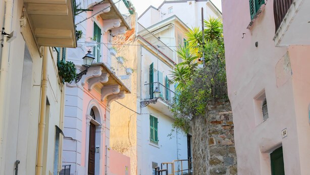 A narrow street with steps leading to a building with a balcony.
