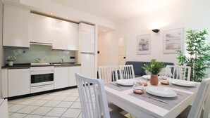 A modern kitchen with white cabinets, a dining table set for four, and a sofa in the background.