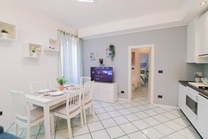 A modern kitchen with white cabinets, a dining area with a white table and chairs, and a TV on a stand.