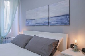 A hotel room with a bed, a nightstand, a lamp, and a wall with three paintings. - SANREMO CASINO' - Centro - Parcheggio (Sanremo)