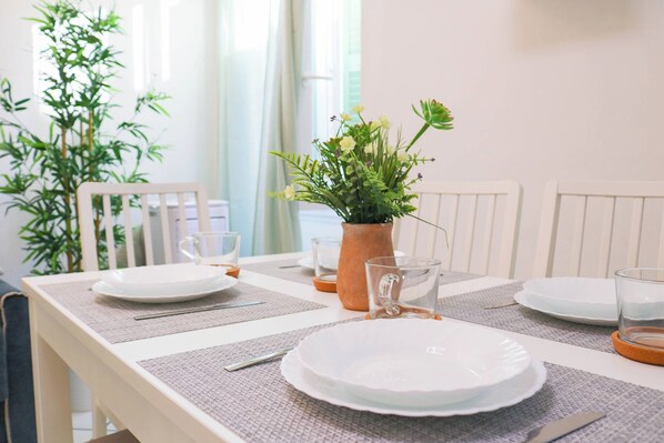 Una mesa de comedor dispuesta con platos, cubiertos y un florero con flores.
