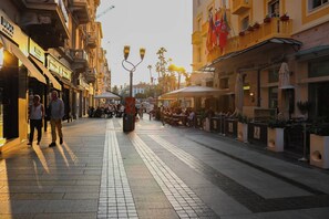Una calle con terrazas, comercios y cielo despejado.